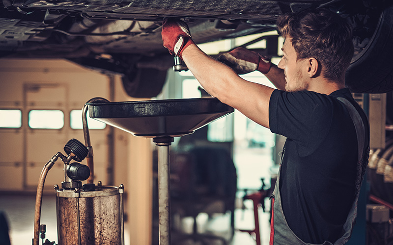 Mechanic performing an oil change under a car.