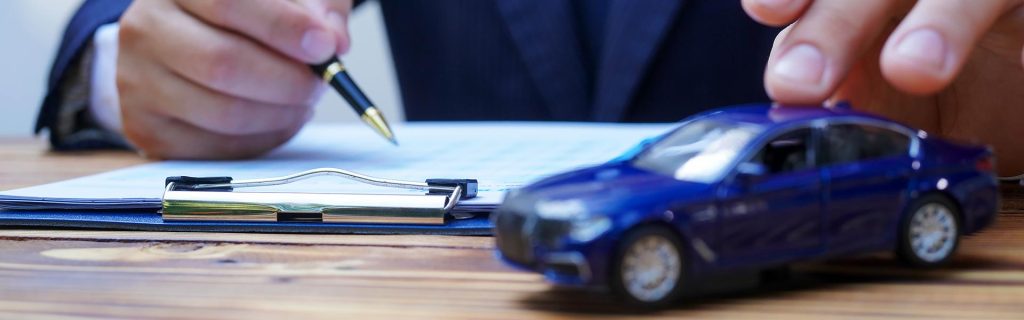 Person signing paperwork next to a toy car.