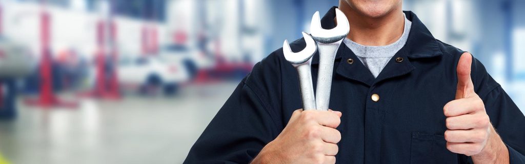 A mechanic holding wrenches and giving a thumbs-up in an auto repair shop.