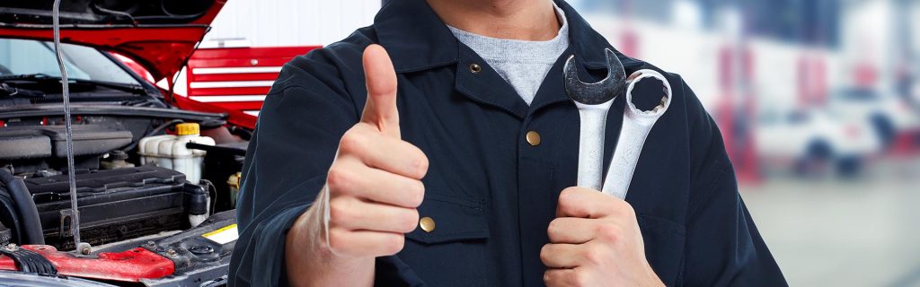 Mechanic holding wrenches and giving a thumbs-up in an auto repair shop