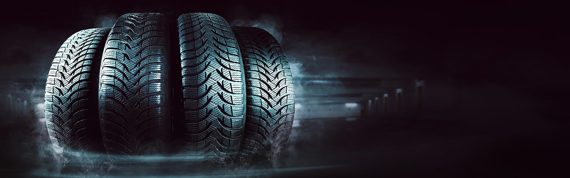 Four car tires displayed against a dark, smoky background
